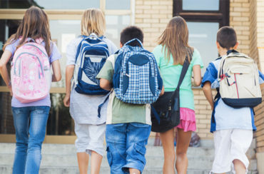 A group of clean children with backpacks walking down the steps.