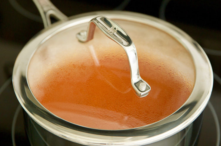 Photo of a covered saucepan of pasta sauce being heated on a stove.