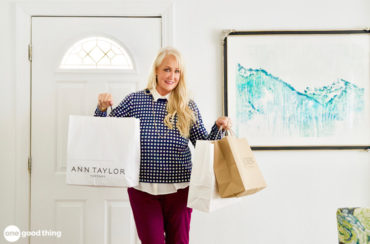 Person holding several shopping bags, standing indoors near a door and a painting.