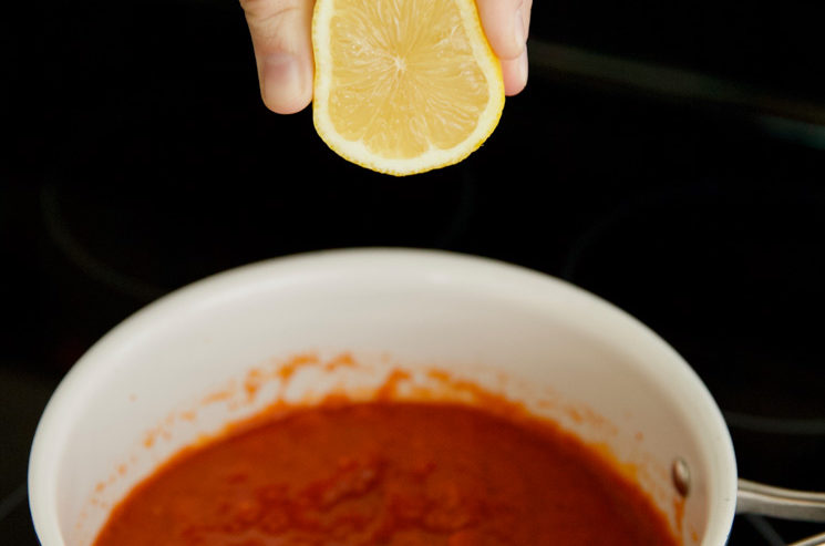 Photo of a hand squeezing a lemon into a saucepan of marinara sauce