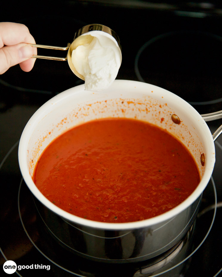 Photo of a person adding sour cream to a pot of pasta sauce