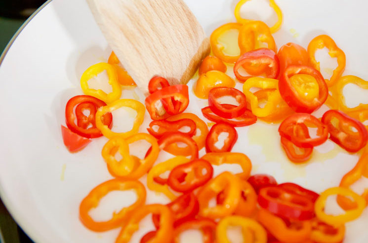 Close up photo of red and yellow pepper rings cooking in a white skillet.