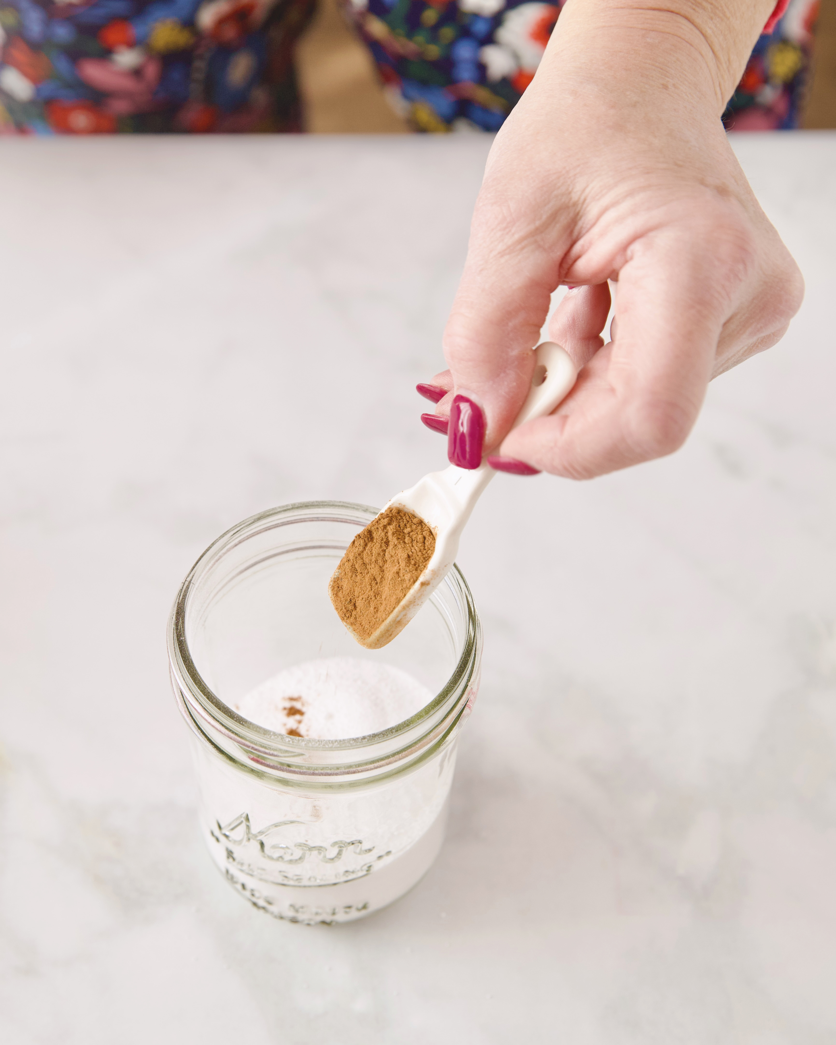 woman's hand putting a spoonful of cinnamon into jar of white powder