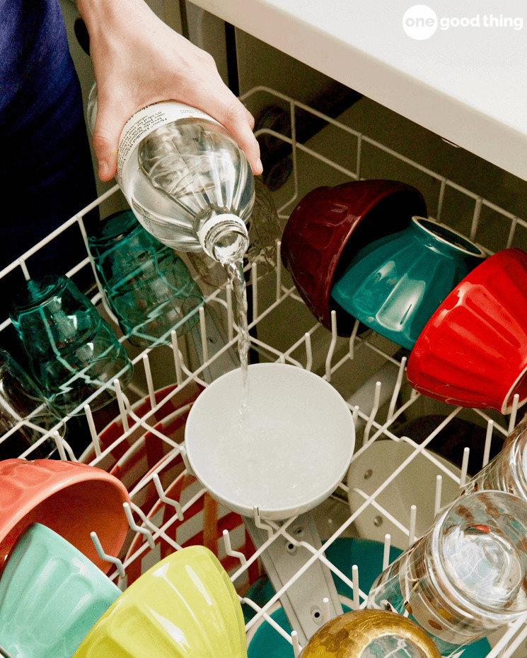 Pouring vinegar into a bowl on the top rack of a dishwasher to prevent stains from hard water in the dishwasher.