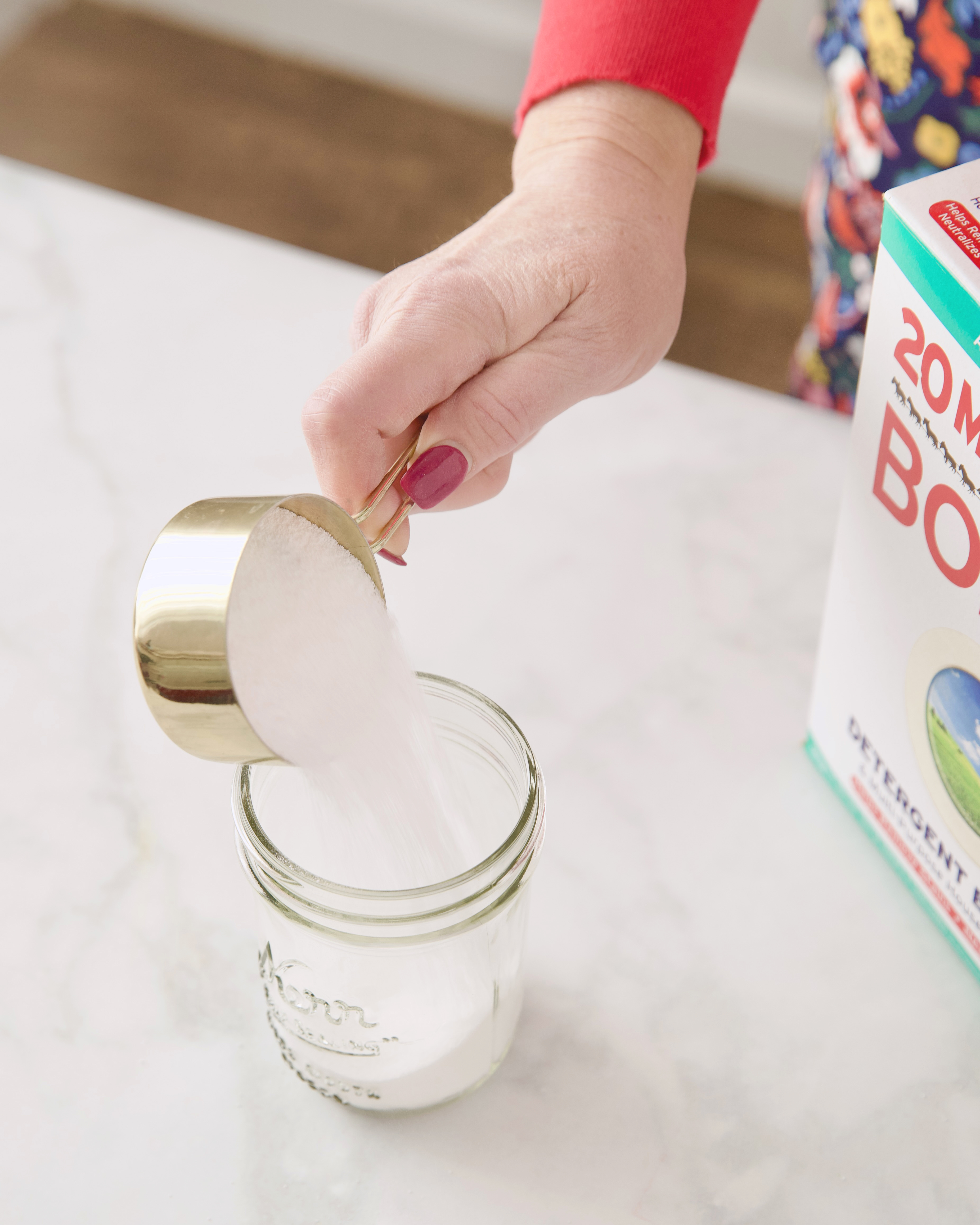 woman's hand pouring borax from measuring cup into jar