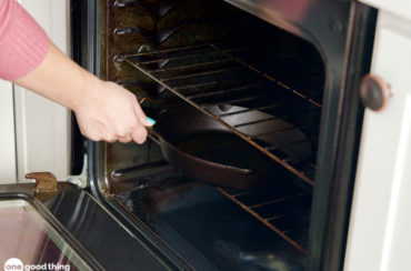 woman's hand putting empty cast iron skillet into oven