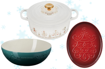 A white Dutch oven by Le Creuset adorned with holiday designs, a teal decorative bowl, and a red oval platter featuring an embossed tree design are elegantly arranged against a backdrop with blue snowflakes, showcasing the Holiday Collection.