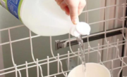 Pouring vinegar into a shallow dish on the top rack of a dishwasher.