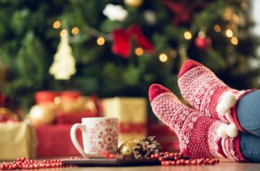 Cozy red socks in front of a decorated Christmas tree with lights and gifts, paired with a mug on a tray filling the air with festive seasonal scents.