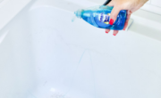 A person using a blue liquid to clean a bathtub for bathtub cleaning.